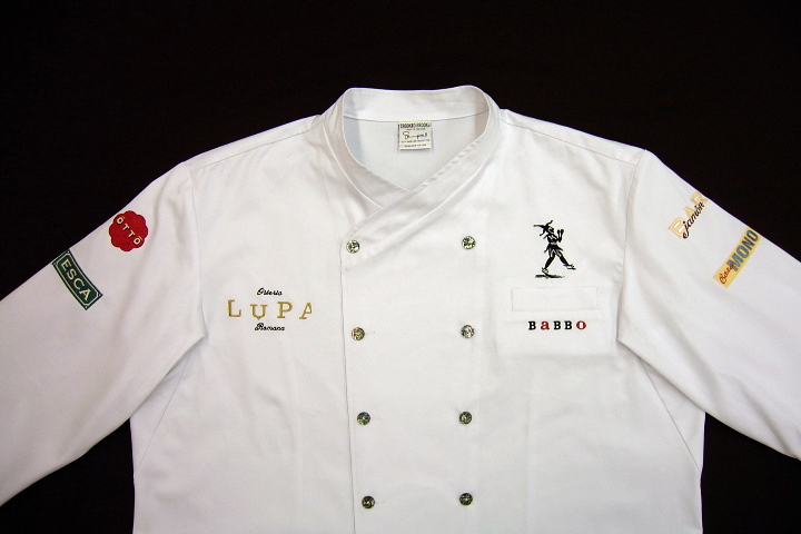 Chef Coat (Jacket) Style CBM101: Shown in white gabardine with Abalone buttons and left chest tailored welt pocket. Embroidered with the logos of Babbo, Lupa, Esca, Otto, Casa Mono, Bar Jamon and Mario Batali's signature on the back.