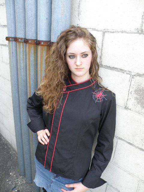 Cropped Women's Jacket Style CBW105H; Shown in black 100% cotton Supima Gabardine with two rows of Foxy Red piping along the collar and placket, one red tagua nut top button, spider embroidery on left front shoulder and square cuffs.