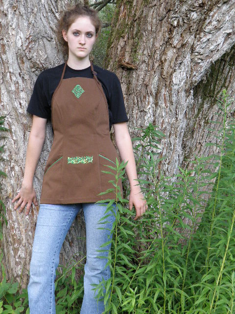 Women's Bib apron style W740 shortened 5 inches; Shown in Nutmeg, 100% cotton denim with two side hip tailored welt pockets, kelly piping on pocket welts, embroidered Celtic Knot on center chest & embroidered vine design on center stomach.