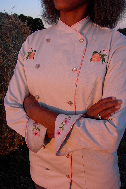 Women's Chef Coat Style BSW101: Shown in Ivory, 100% cotton Denim, bisque piping (collar, front & cuffs), Peach botanicals (one embroidered on each chest), peach blossom chains (one embroidered on each cuff) & awabi buttons.