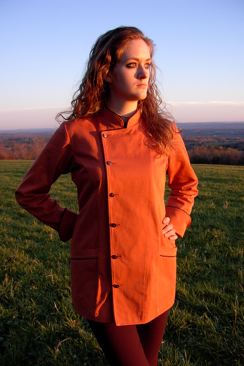 Women's Chef Coat Style BSW102: Shown in Terra Cotta, 100% cotton denim, black piping (collar, front, cuffs & pockets), two front hip tailored welt pockets, kissing collar & pin shank buttons.