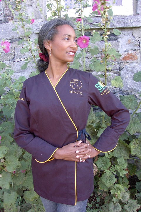 Women's Chef Coat Style BSW106: Shown in navy, 100% cotton gabardine, Scholastic piping (cuffs, collar & front). Embroidered with the logos of Rialto, Share Our Strength & Kitchen Divas 9.19.05.